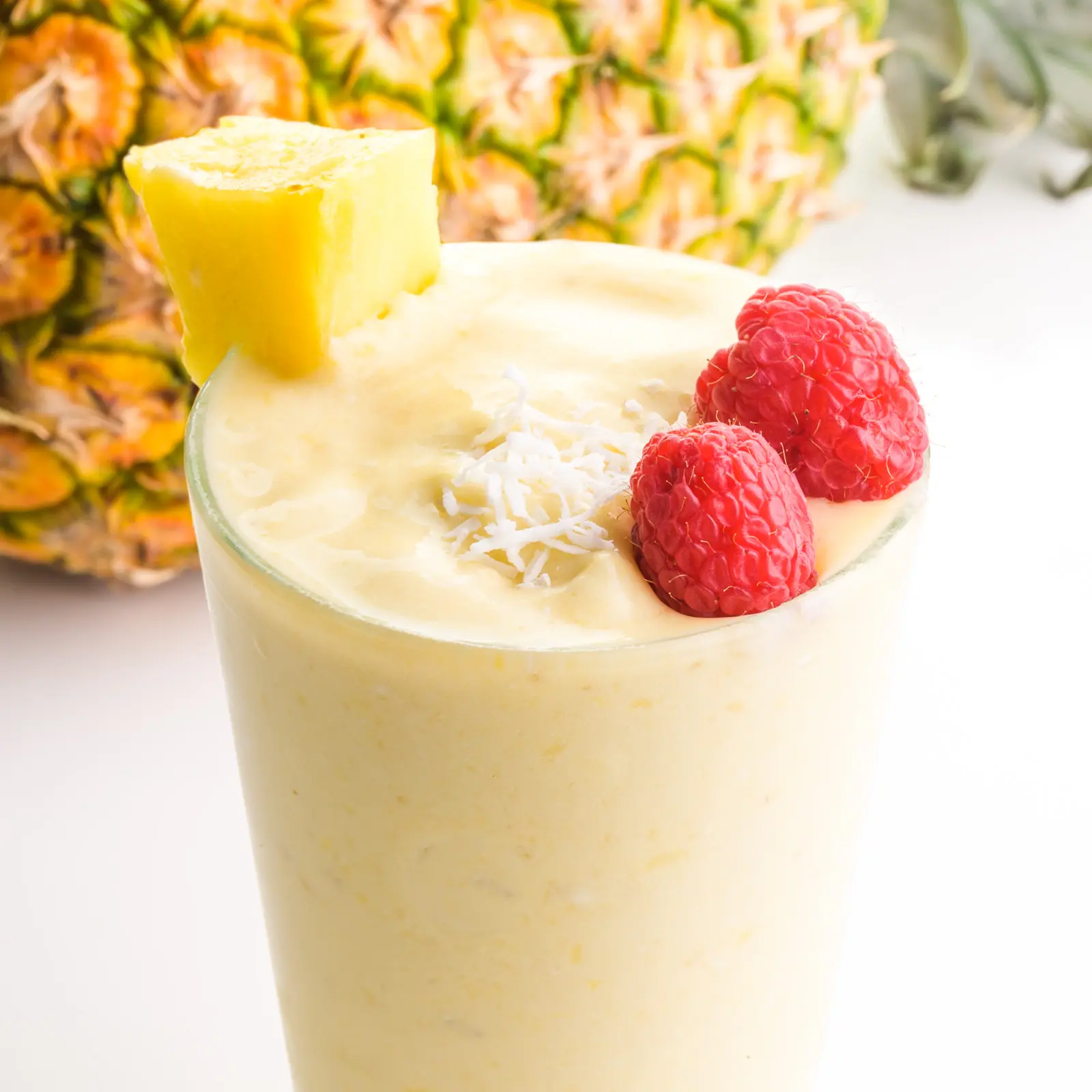 A glass of Pina colada smoothie has fresh raspberries, coconut flakes, and other fresh fruit.