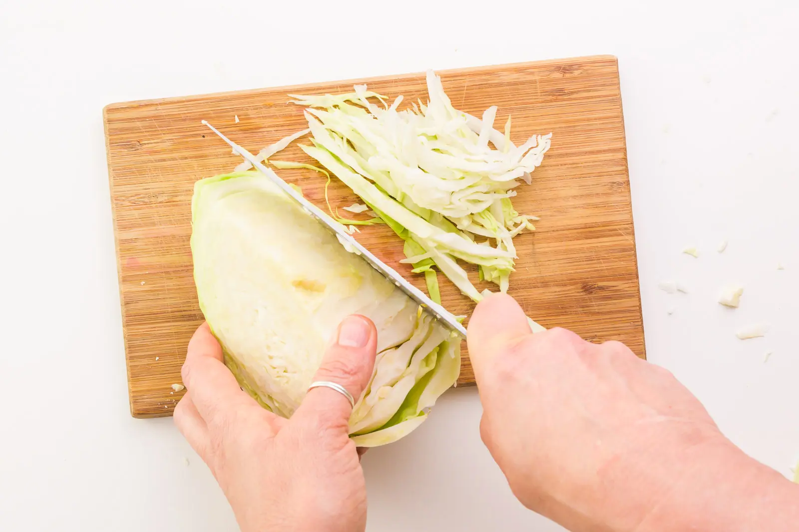 Looking down on a hand holding a chef's knife, shredding cabbage on a cutting board.