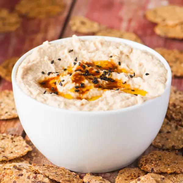 A bowl full of smoky chipotle hummus is surrounded by crackers.