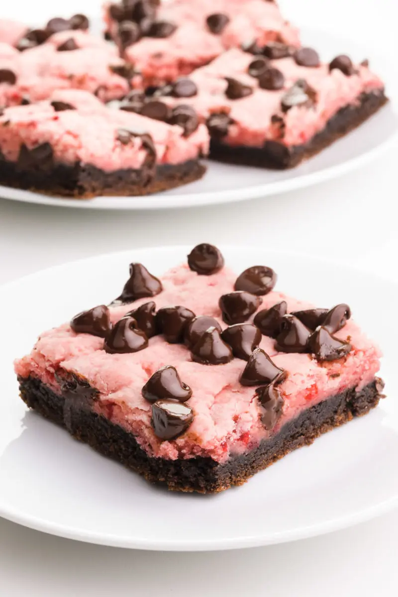 A strawberry chocolate bar sits on a plate.  It has lots of melted chocolate chips on top. There is another plate with several more bars in the background.