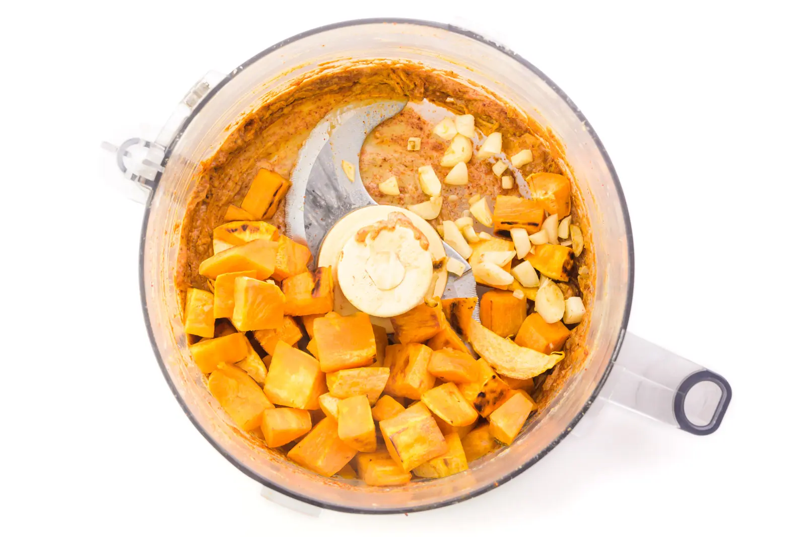 Ingredients are in a food processor, such as sweet potatoes, garlic, and other ground up ingredients.