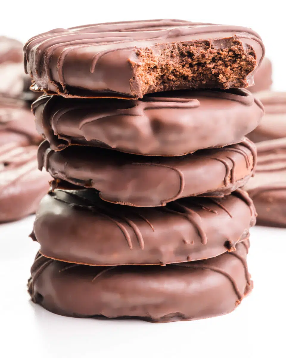 A stack of vegan chocolate mint cookies shows the top one with a bite taken out. There are more cookies in the background.