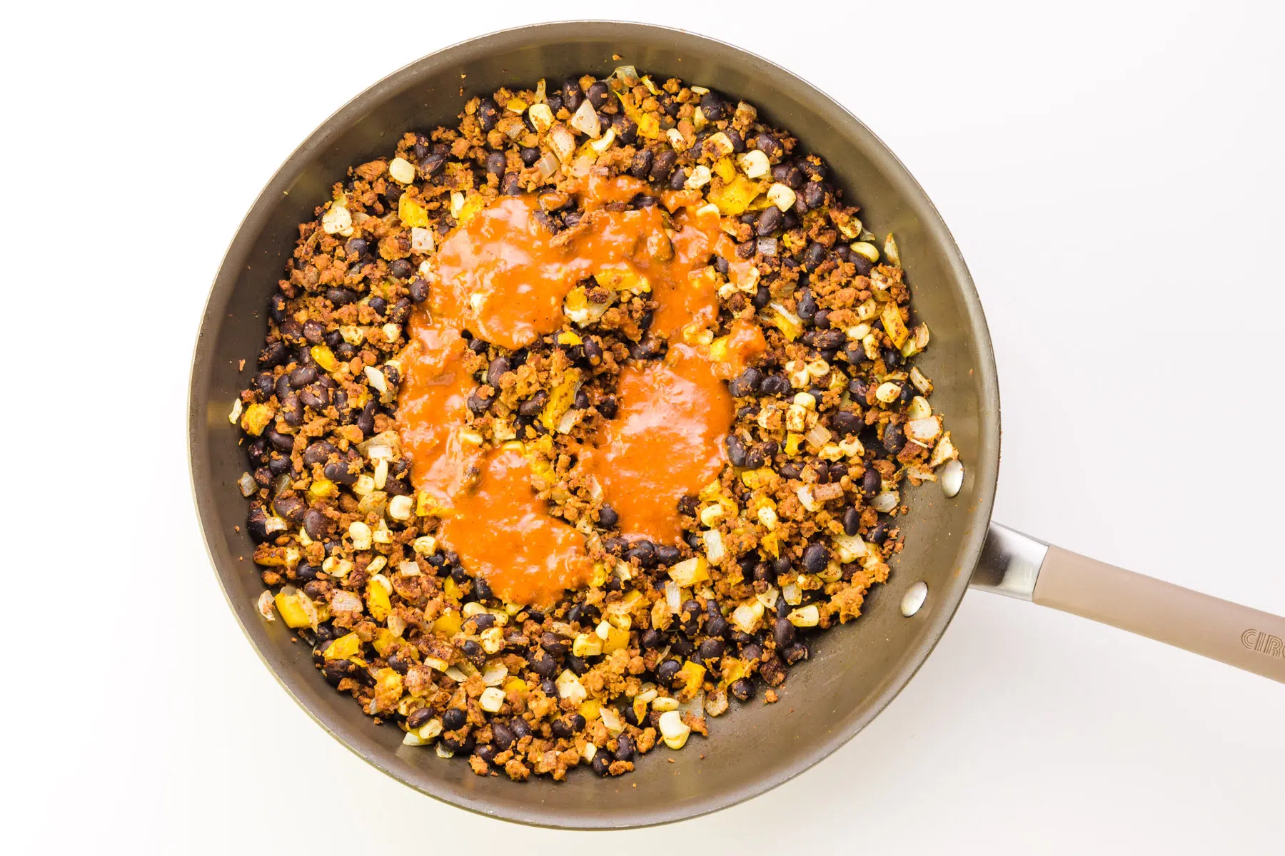 A veggie crumble mixture is cooking in a skillet. There is enchilada sauce drizzled over the top.