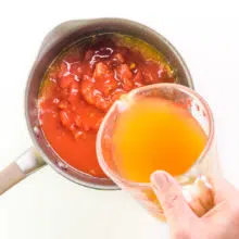 Vegetable broth is being poured into a saucepan with tomatoes and other vegetables.