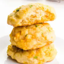 A stack of vegan cheddar bay biscuits shows the top one with a bite taken out. There are more biscuits in the background.