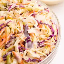 Looking down on the right side of a bowl of coleslaw with a bowl of more coleslaw sauce in the background.