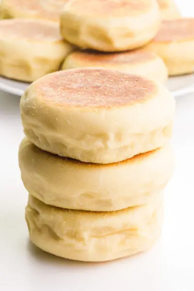 A stack of 3 vegan English muffins is in front of a wire rack with more muffins.