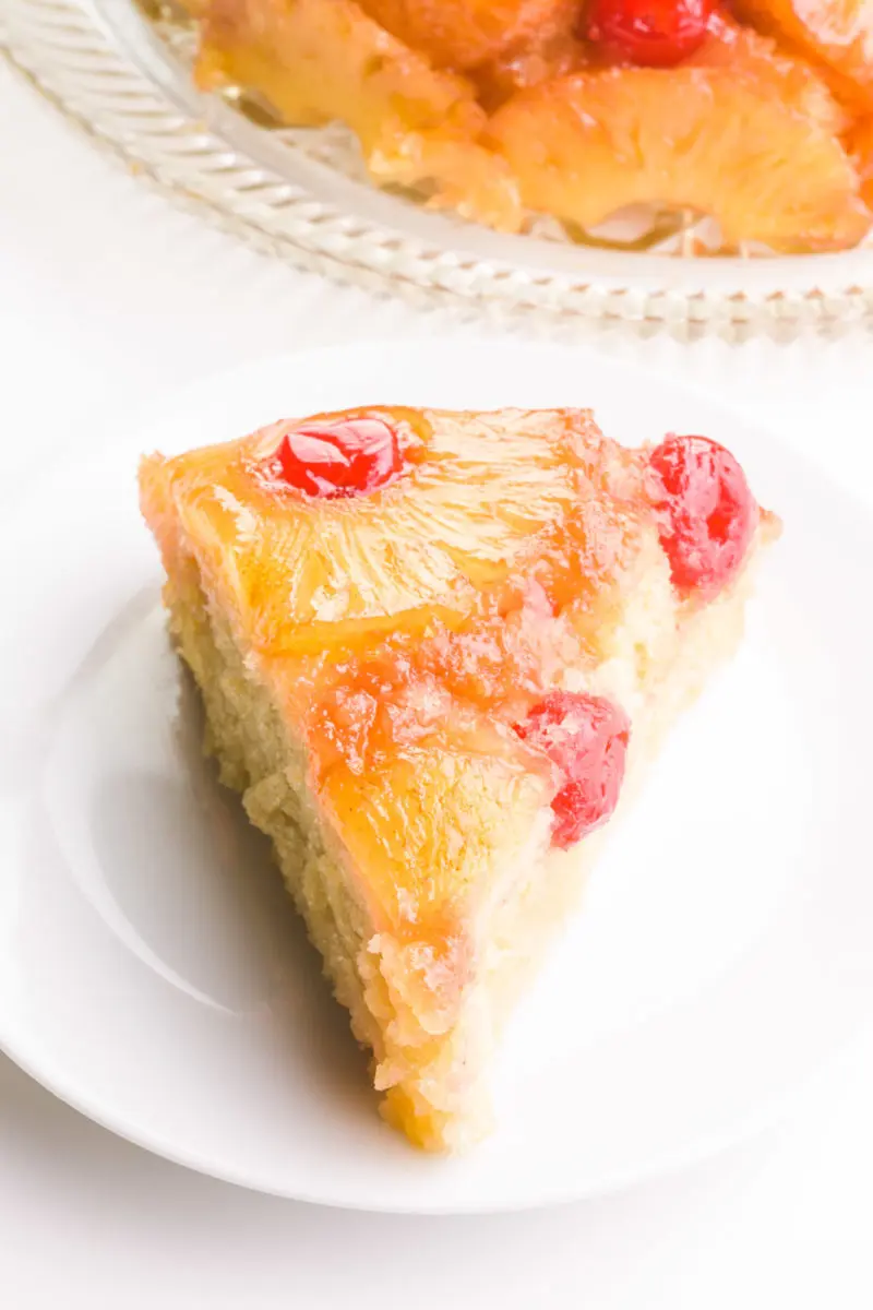 A slice of vegan pineapple upside down cake shows pineapples and maraschino cherries on top. The rest of the cake is behind it.