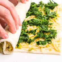 Hands are rolling up pastry with a spinach and cheese filling.