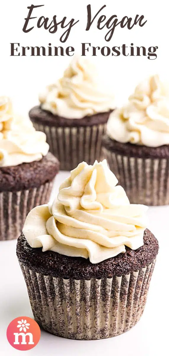 A cupcake has a tall dollop of creamy white frosting on top. There are several frosted cupcakes in the background. The text at the top of the image reads, Easy Vegan Ermine Frosting.