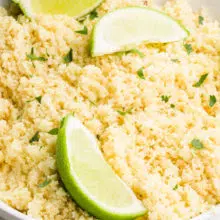 A bowl has riced cauliflower in it and there are lime wedges on top.