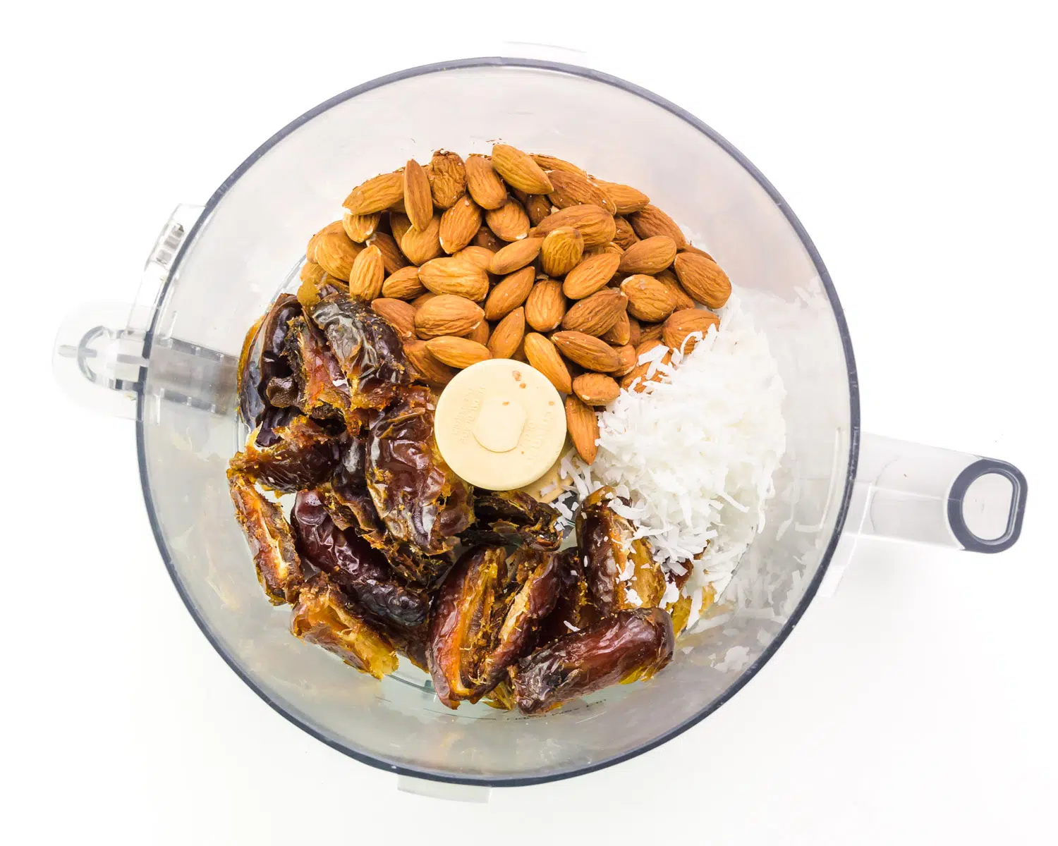 Looking down on a food processor with raw almonds, dates, and coconut flakes.