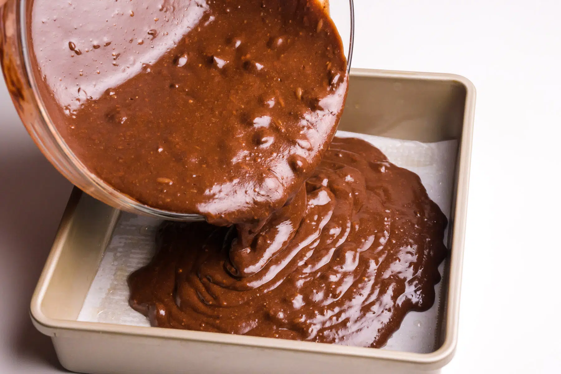 Brownie batter is being poured into a baking dish.