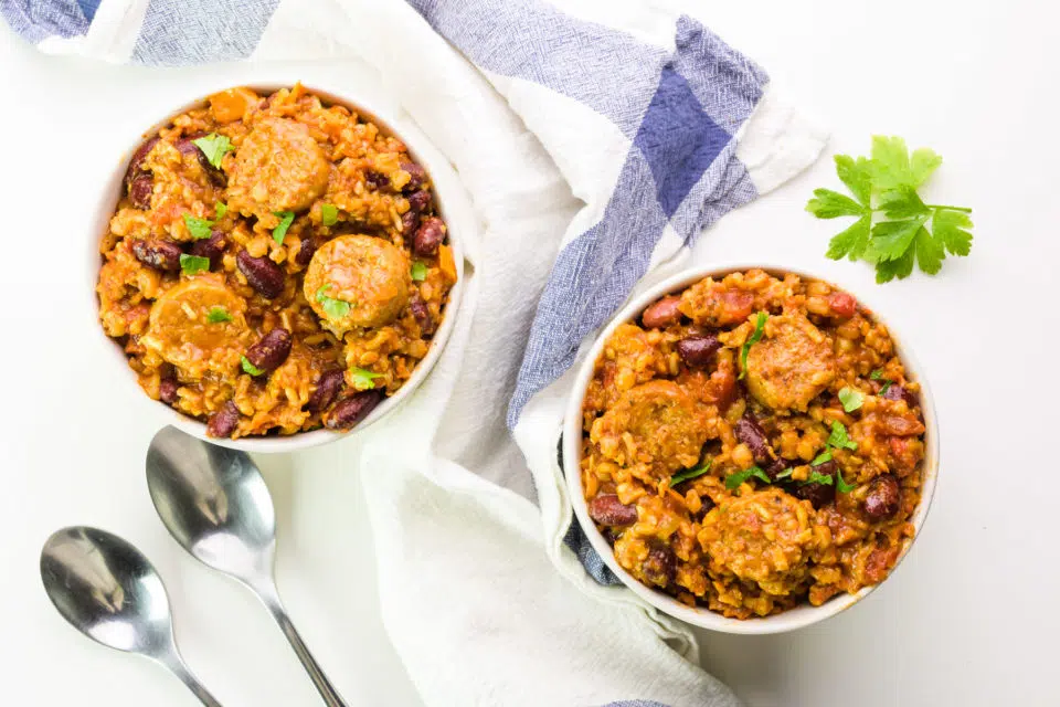 Looking down on two bowls full of meatless jambalaya with a kitchen towel between them and two spoons beside them.