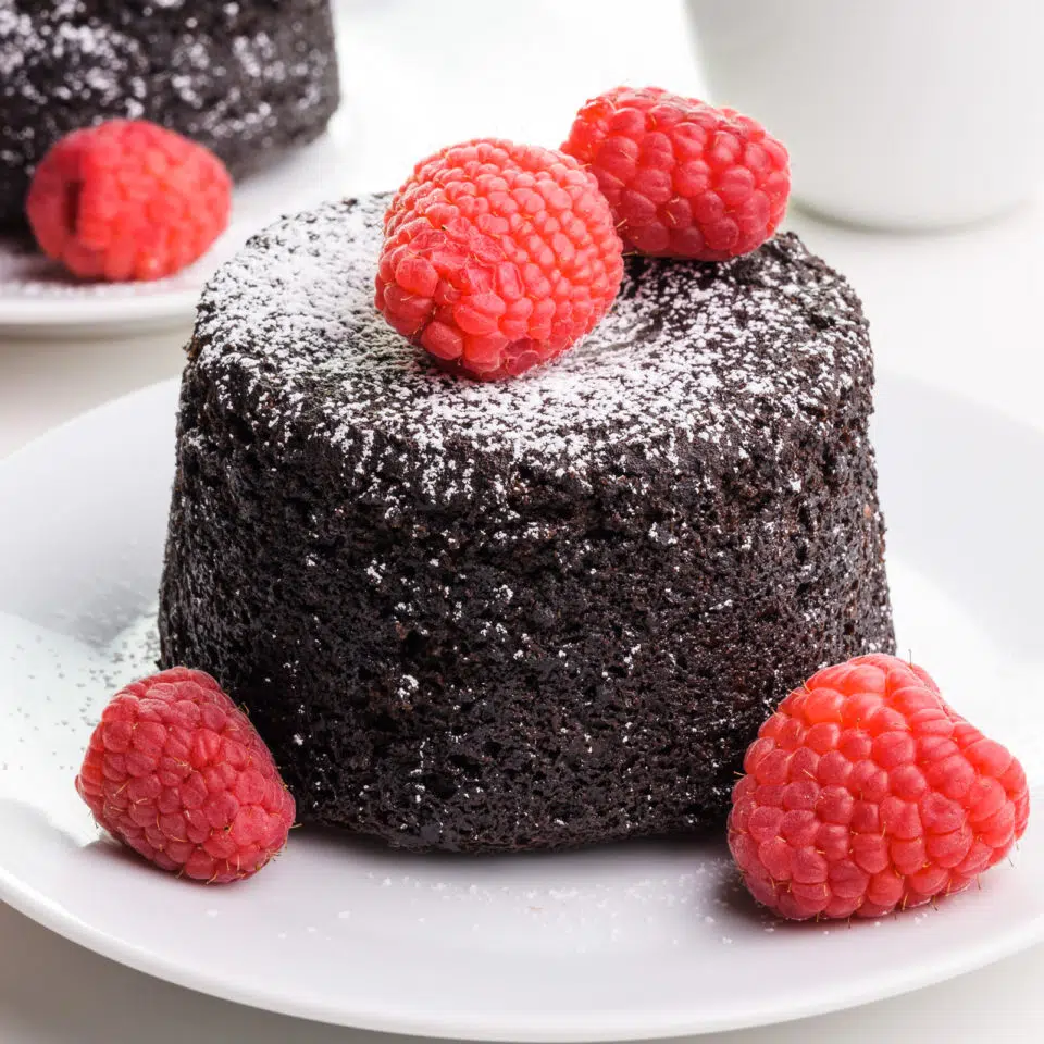 A vegan lava cake has powdered sugar and raspberries on top.