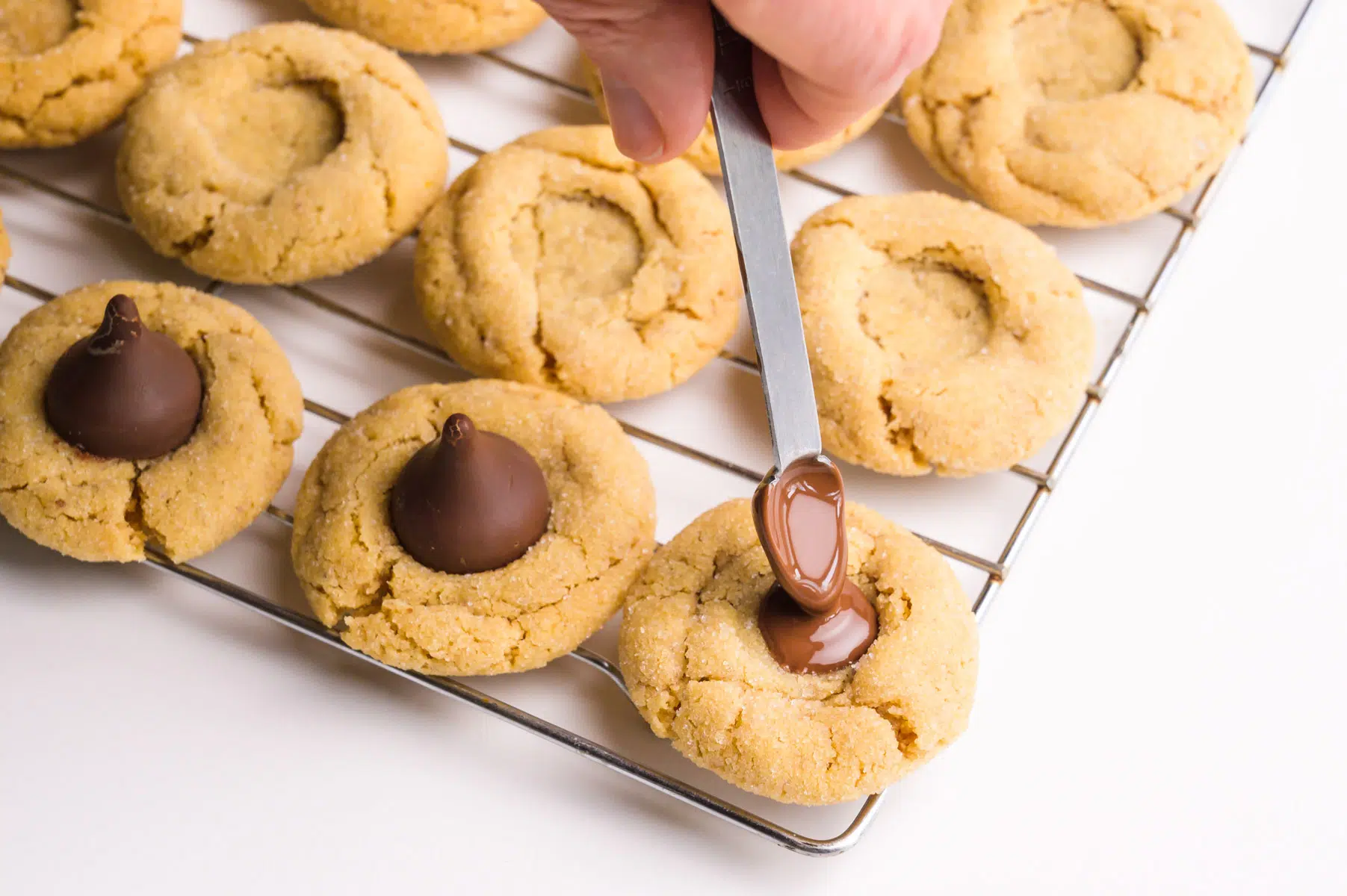 Melted chocolate is being poured into a divot in the center of peanut butter cookies.