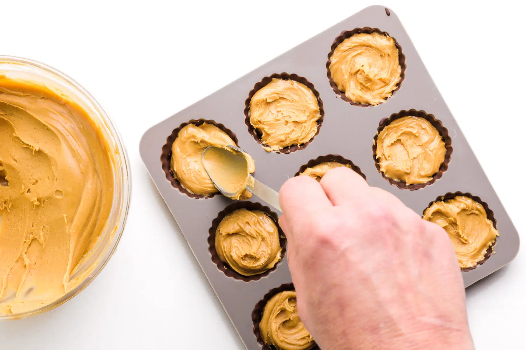 A hand holds a spoon pressing peanut butter over set chocolate in candy molds.
