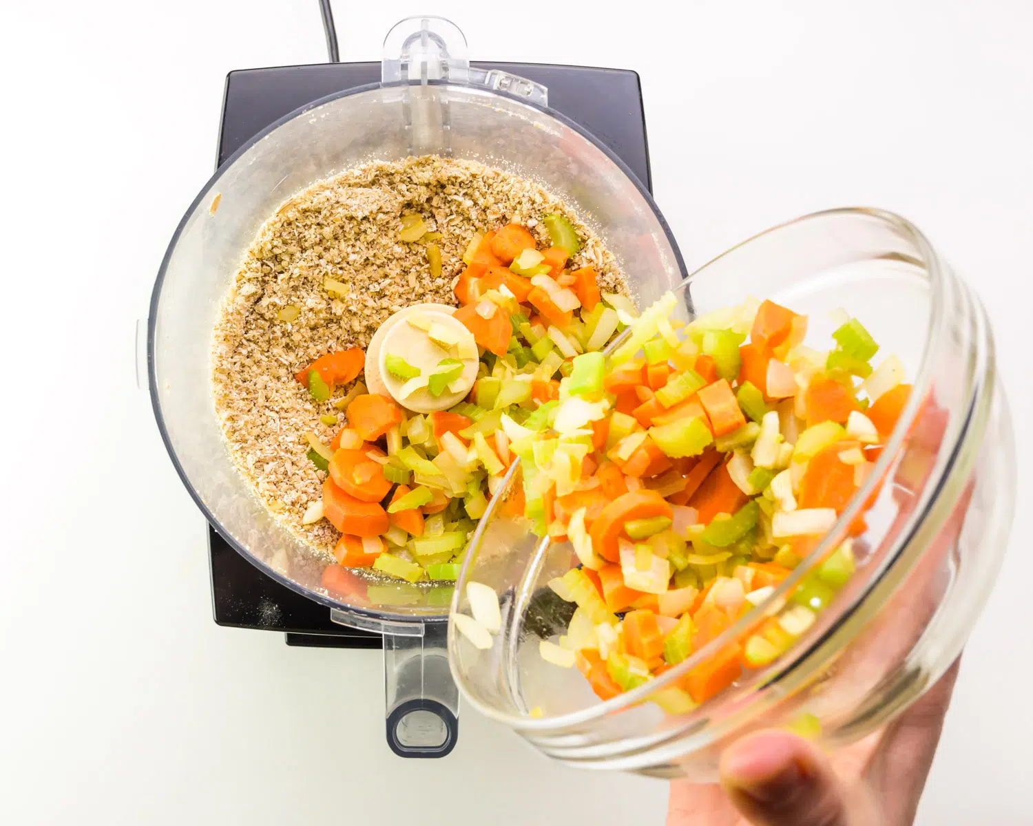 Cooked vegetables are being added to a food processor with other ingredients.
