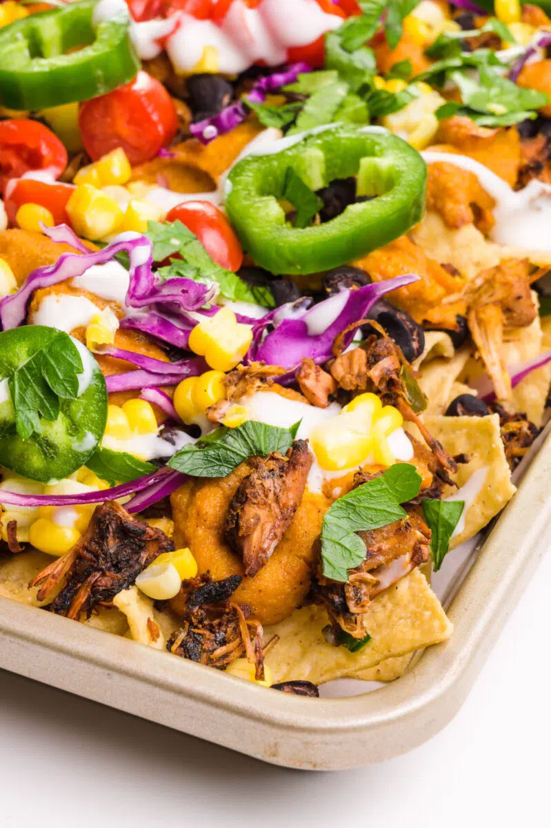 A baking sheet holds nachos with jackfruit carnitas, red cabbage, and jalapeños on top.