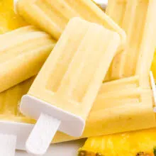 A plate of pineapple popsicles has sliced pineapple wedges on it too.