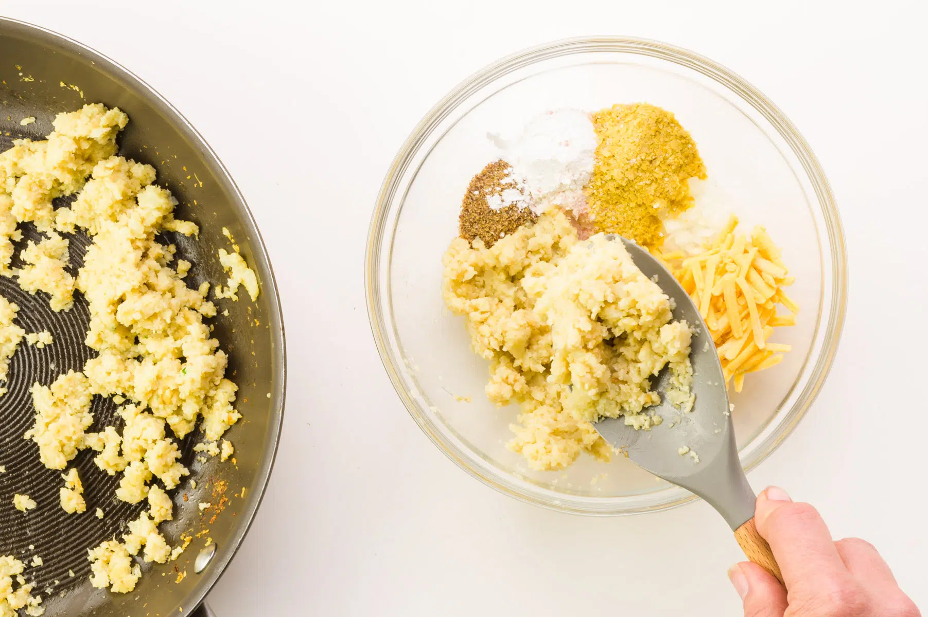 A hand holds a spatula, adding cooked cauliflower rice to a bowl with other ingredients.