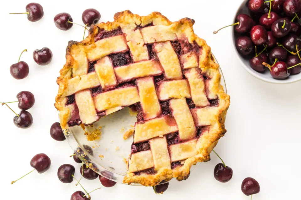 Looking down on a lattice-crust cherry pie with fresh cherries and a bowl of fresh cherries beside it.
