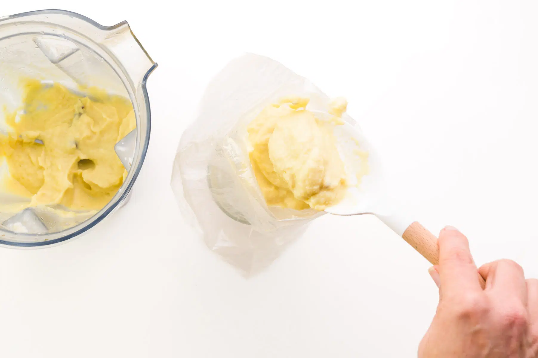 A hand holds a spatula, transferring dole whip from a blender to a piping bag.