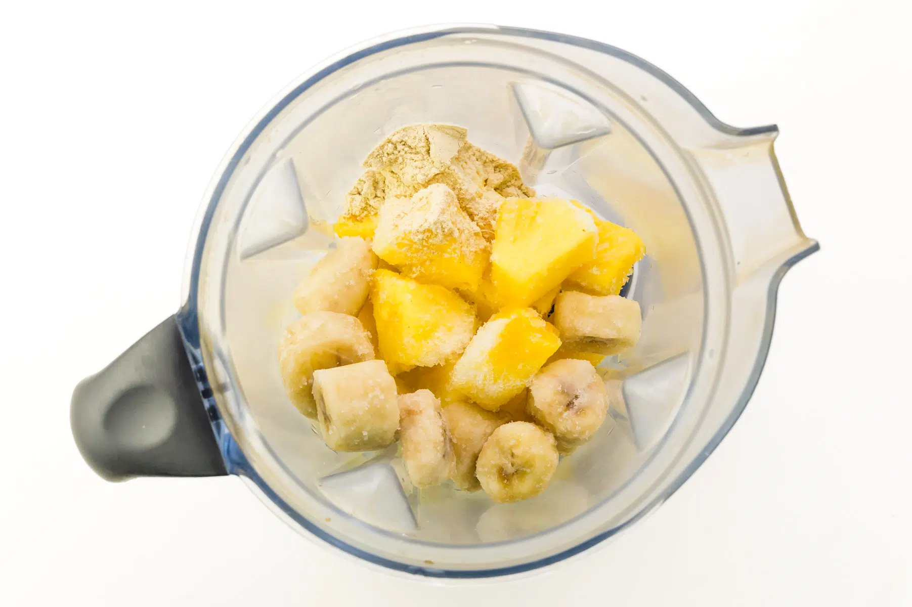 Frozen pineapple and banana chunks are in a blender jar.