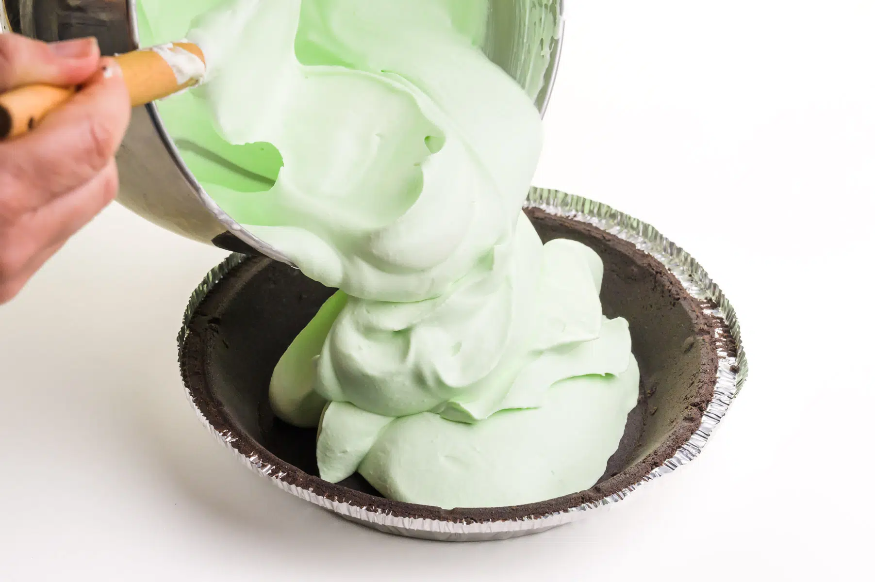 Green whipped mousse is being poured into a chocolate pie crust.