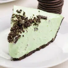 A slice of vegan grasshopper pie sits on a plate with chocolate sandwich cookies visible in the background.