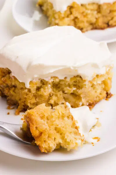 A bite of dairy-free pineapple cake sits on a fork in front of the rest of the cake slice. There's another slice in the background.