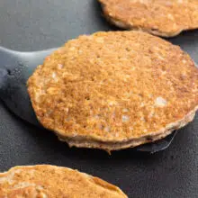 A spatula holds a pancake on a griddle, getting ready to flip it. There are other pancakes on the griddle, too.