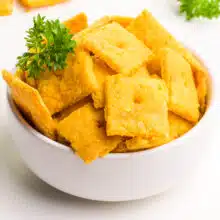 A bowl of vegan gluten-free cheez-its are in a bowl with a spring of parsley.