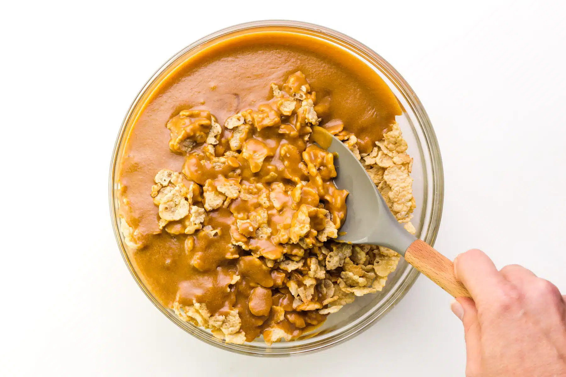 A hand holds a spatula stirring peanut butter and cereal together.