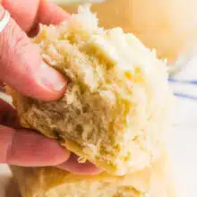 A hand holds a vegan dinner rolls with a bit of butter on top.