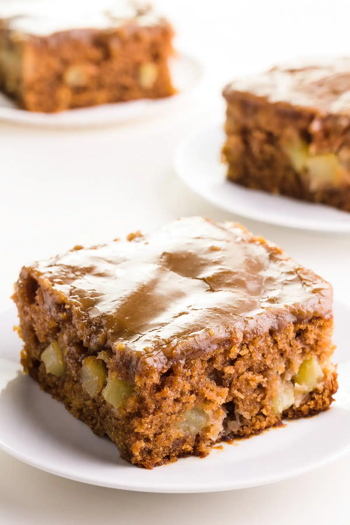 A slice of vegan apple cake sits on a plate in front of other slices in the background.