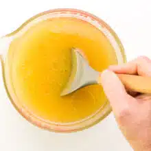 A hand holds a spatula, stirring a mixture of water, applesauce, and other ingredients.