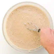 A hand holds a whisk stirring cake batter in a bowl.