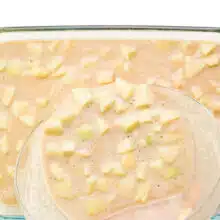 Cake batter with apple bits is being poured into a 9x13 cake pan.