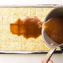 A caramel mixture is being poured over crackers in a pan.