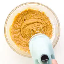 An electric mixer is beating a peanut butter mixture in a bowl.