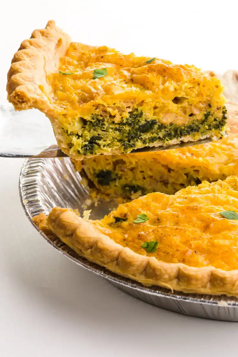 A slice of quiche is on a spatula, hovering over the rest of the quiche.