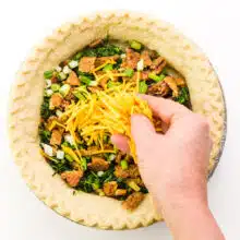 A hand spread vegan cheese across a pie crust with spinach and other ingredients.