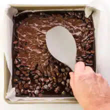 A hand holds a spatula, spreading melting chocolate chips in a pan.