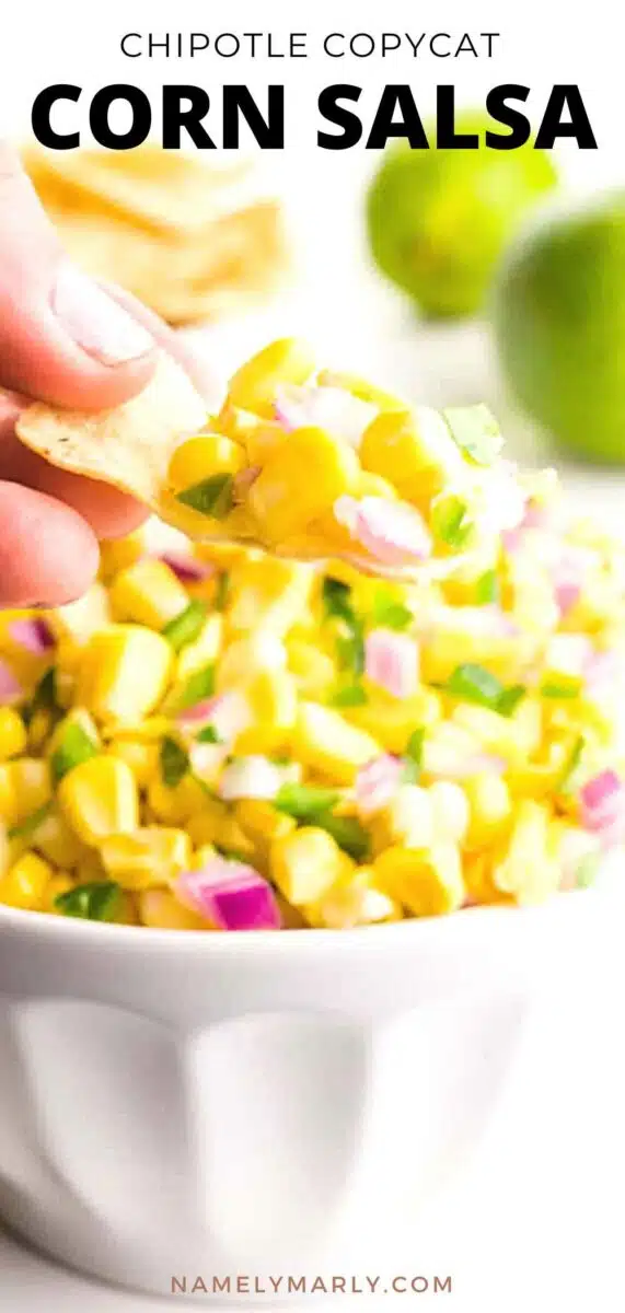A hand holds a chip full of corn hovering over a bowl with more corn. There are limes in the background. The text reads, Chipotle Copycat Corn Salsa.