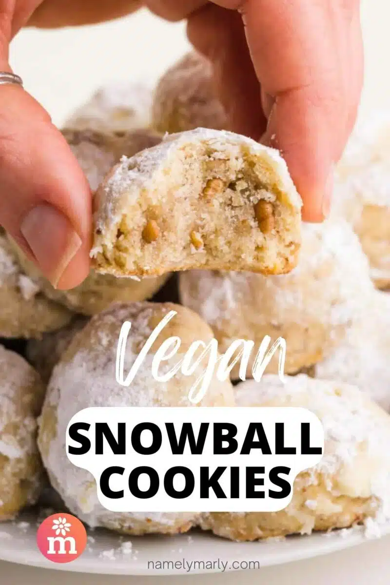 A hand holds a cookie with a bite out in front of a tray of cookies. The text reads, Vegan Snowball Cookies.