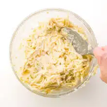 A hand holds a spatula, stirring potatoes with a creamy mixture.