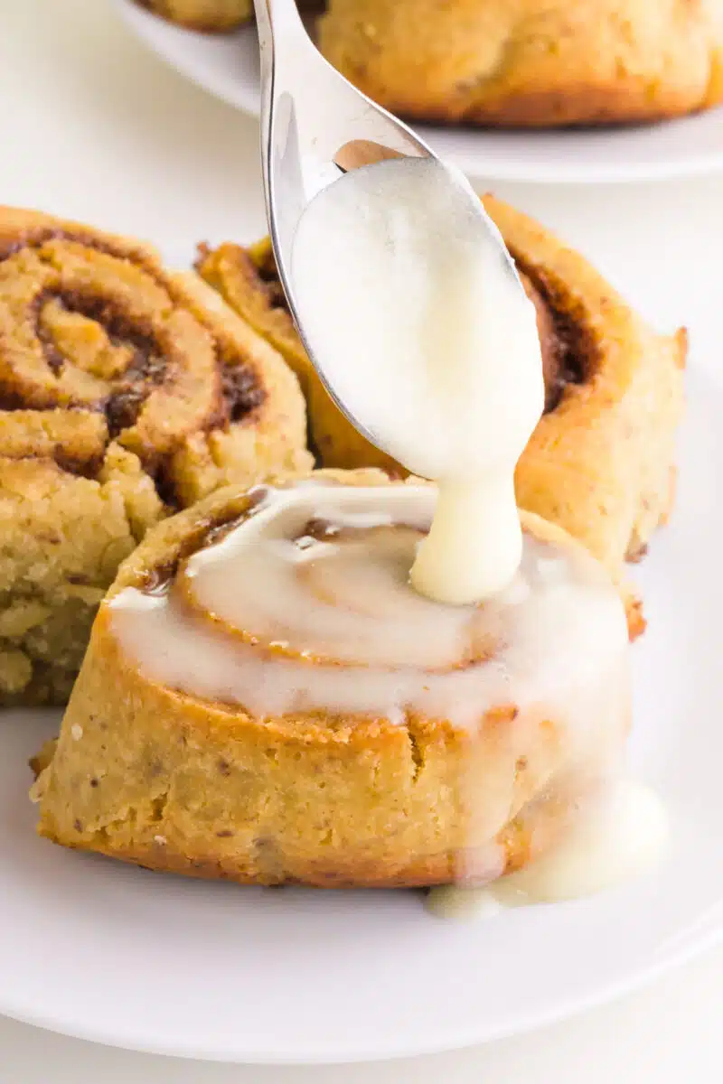 A spoon drizzles icing over vegan gluten-free cinnamon rolls.
