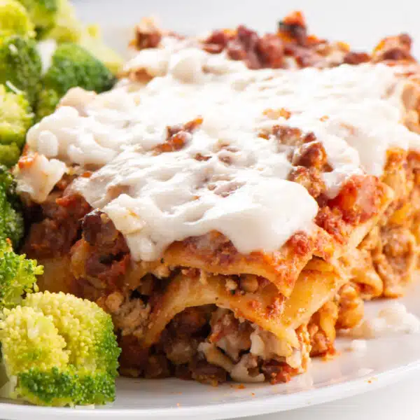 A closeup of vegan lasagna on a plate. There is steamed broccoli next to it.