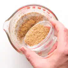 A hand holds a bowl of ground flax, pouring into a bowl with chia pudding.